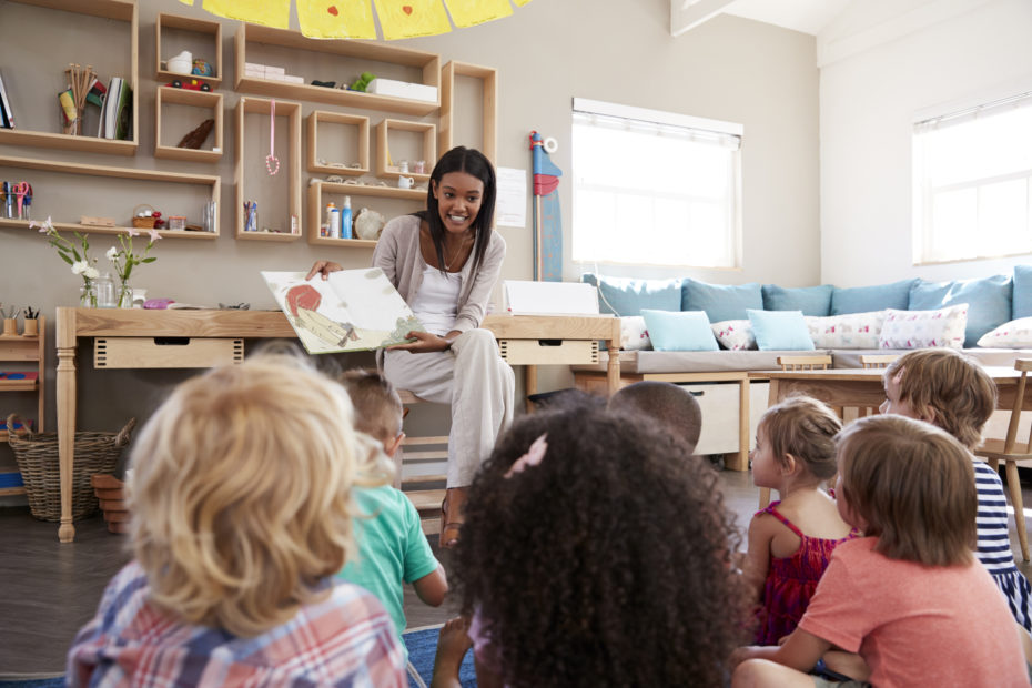 teacher in front of a classroom of students reads a book